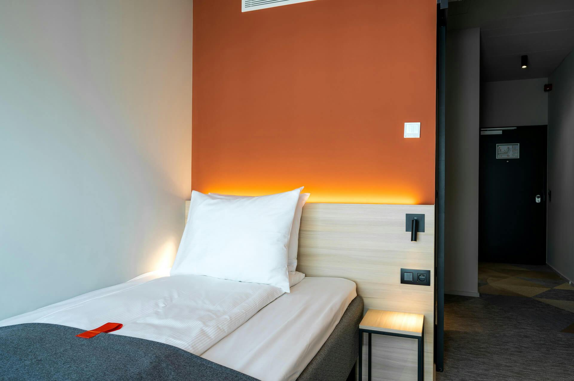 Single bed, orange wall, reading lamp, hallway, door