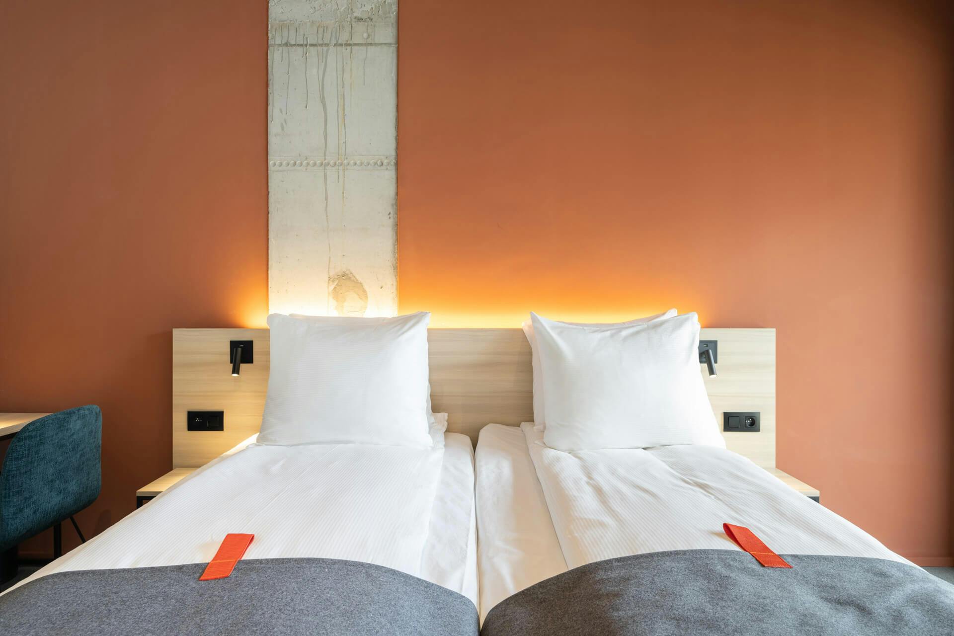 Twin beds, orange wall, chair, desk