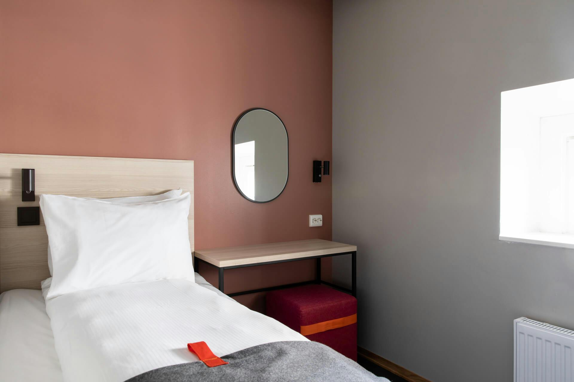 Single bed, desk, mirror, poof, orange wall