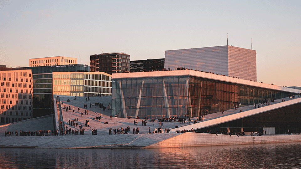 Image of the Opera House in Oslo at sunset. It has an angled exterior surface with white granite.